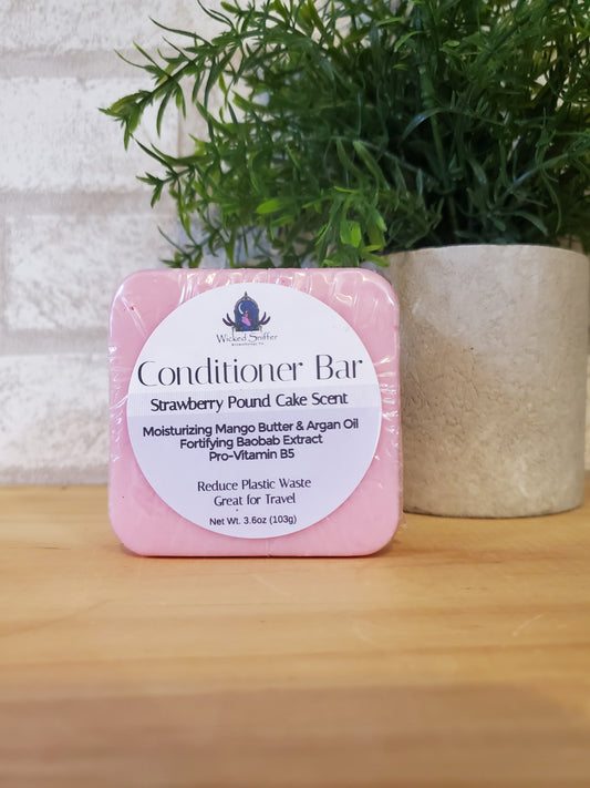 Pink conditioner bar with a label on a wooden surface next to green plants