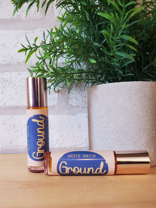 Two 'Ground' rollerball bottles on a textured surface with a plant in the background
