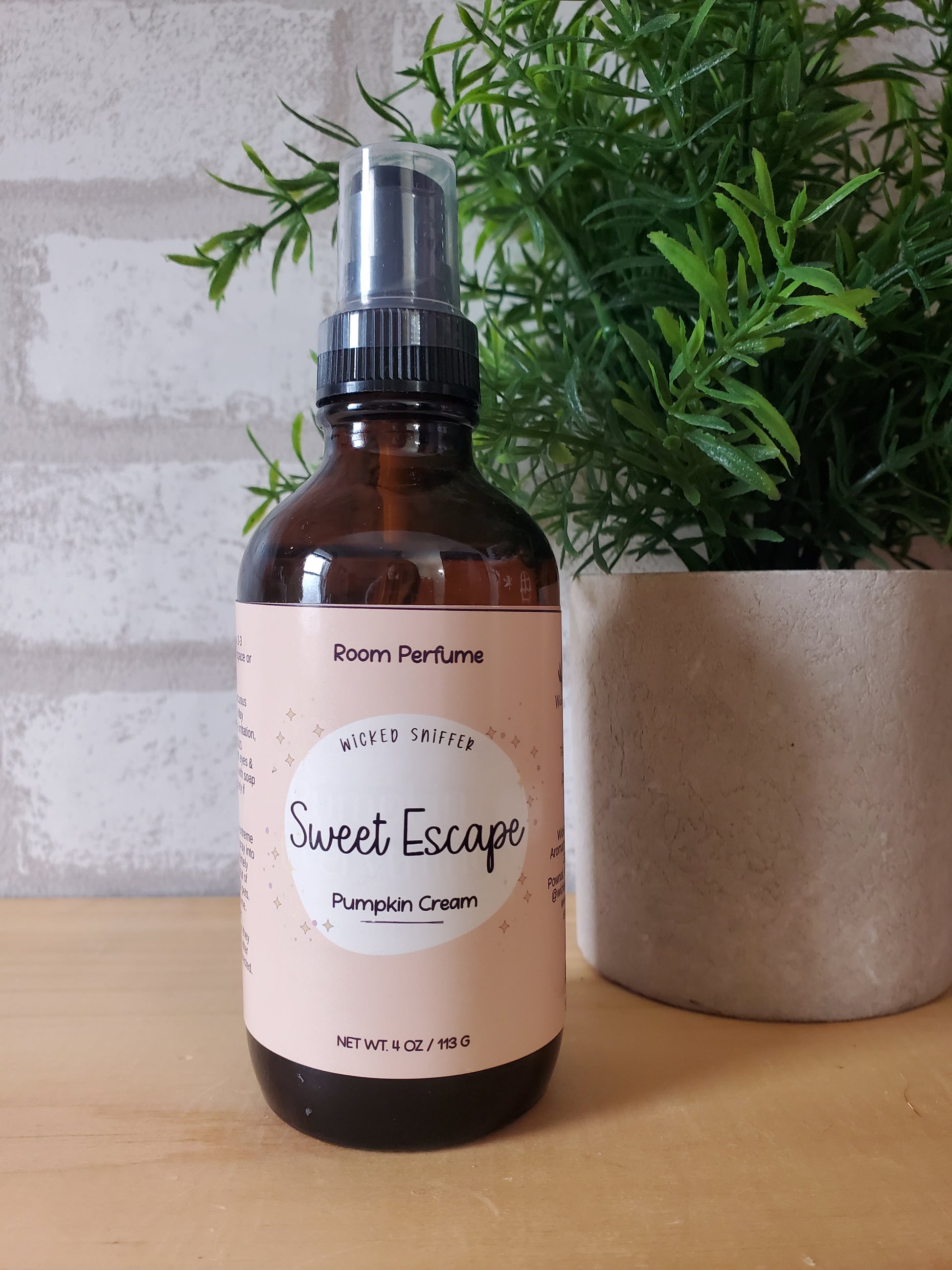 Bottle of 'Sweet Escape' room perfume with a plant in the background