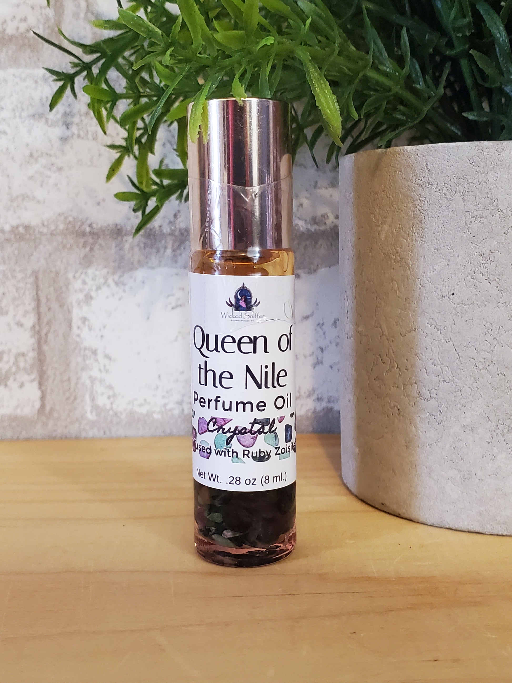Perfume bottle labeled 'Queen of the Nile' on a textured surface with greenery.
