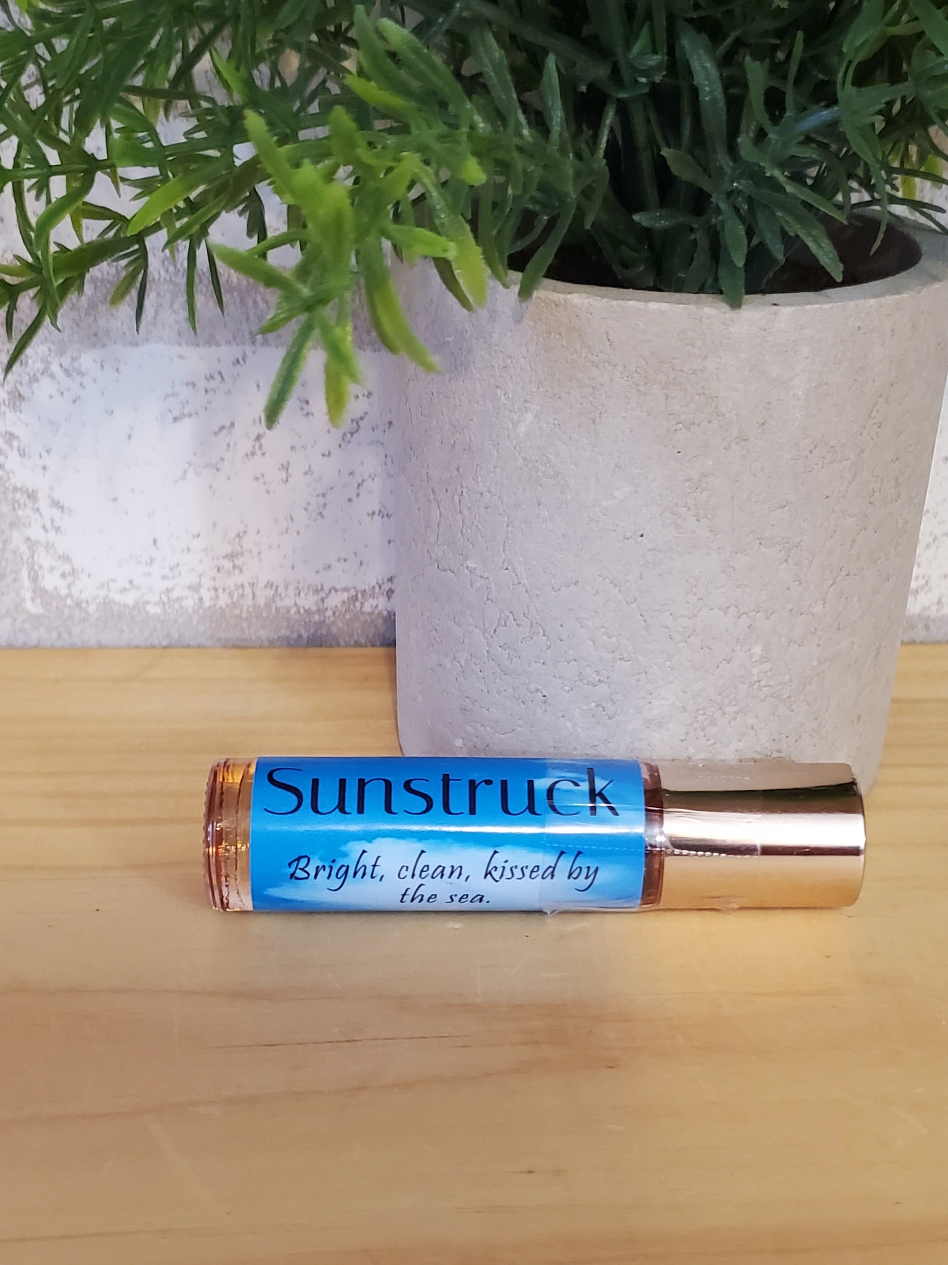 Roll-on bottle of Sunstruck perfume oil on a wooden surface with a plant in the background