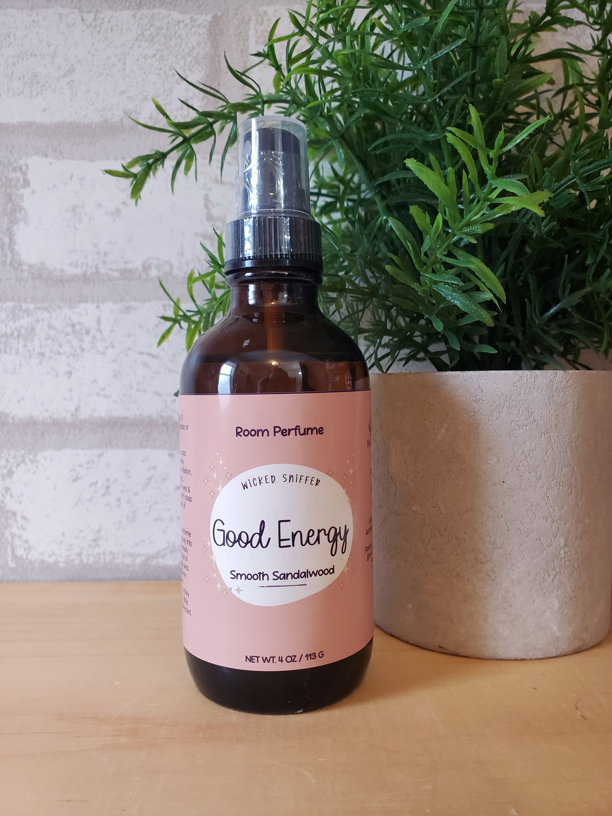 Bottle of room perfume with a pink label on a textured surface with greenery