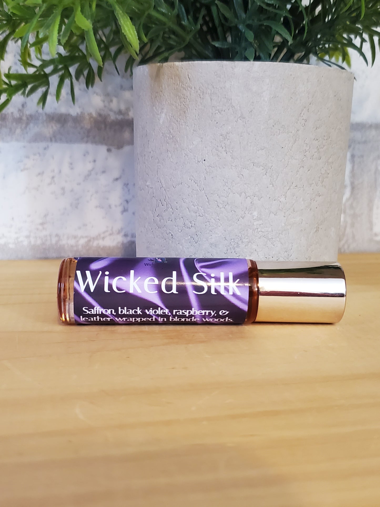 Roll-on bottle of 'Wicked Silk' on a wooden surface with greenery in the background