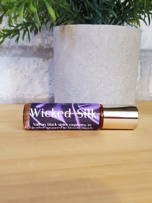 Roll-on bottle of 'Wicked Silk' on a wooden surface with greenery in the background