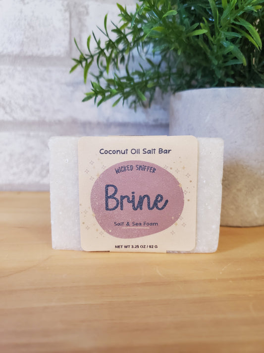 Bar of soap with a visible brand label on a wooden surface next to greenery