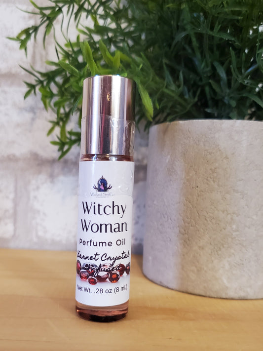 Perfume oil bottle labeled 'Witchy Woman' on a wooden surface with greenery in the background