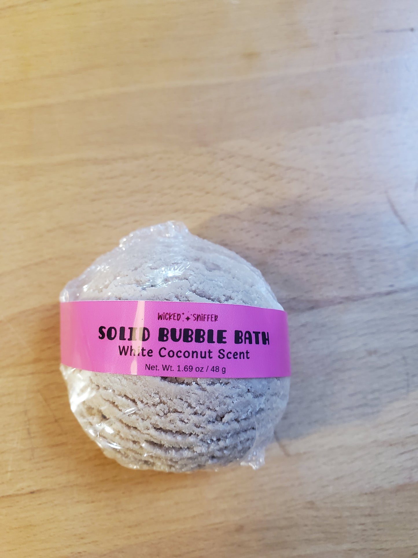 Solid bubble bath scoop with a pink label on a wooden surface