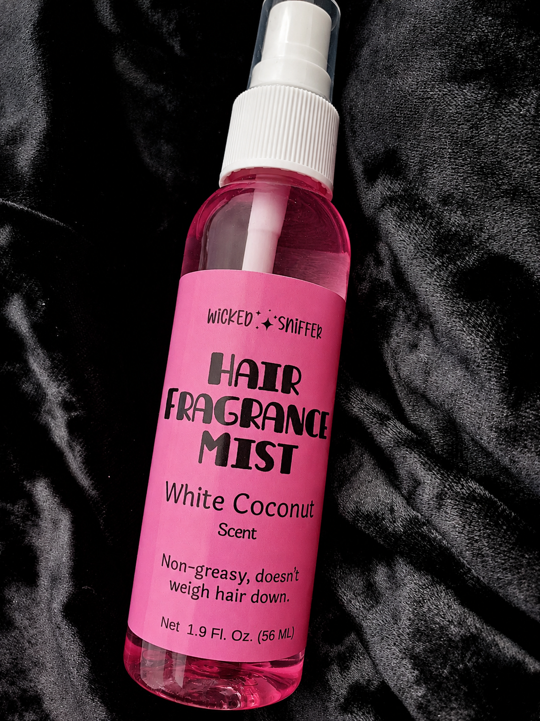 Pink hair fragrance mist bottle with white cap on a black textured background