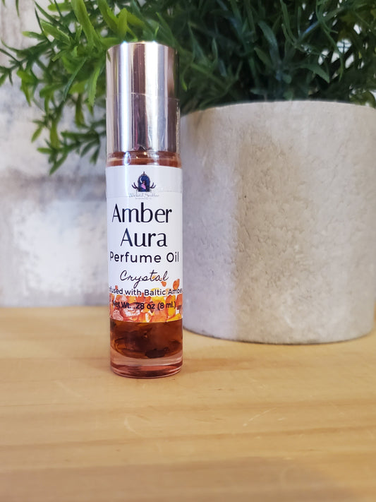 Perfume oil bottle labeled 'Amber Aura' on a wooden surface with greenery.