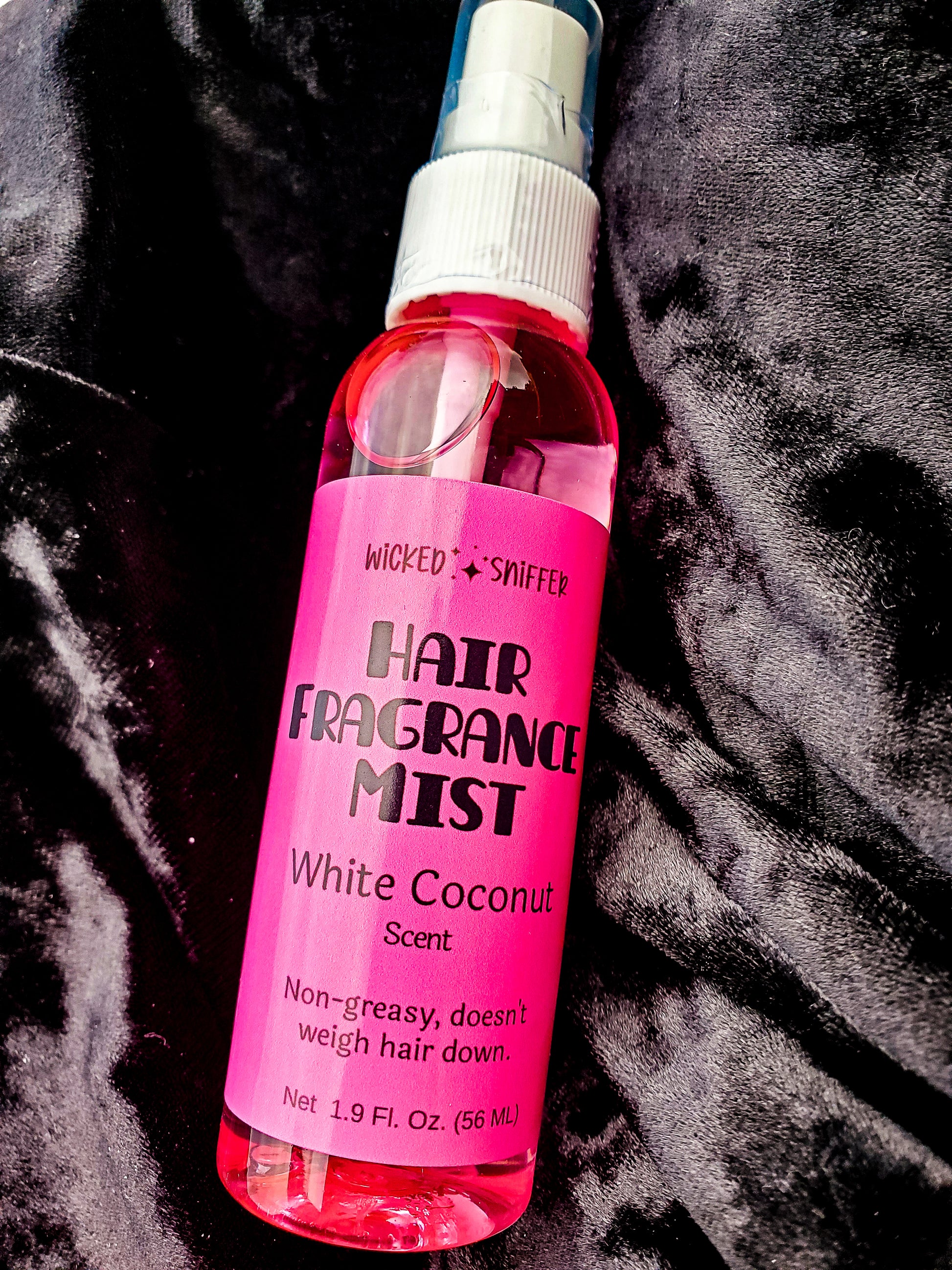 Pink hair fragrance mist bottle with a pink label on a dark textured background