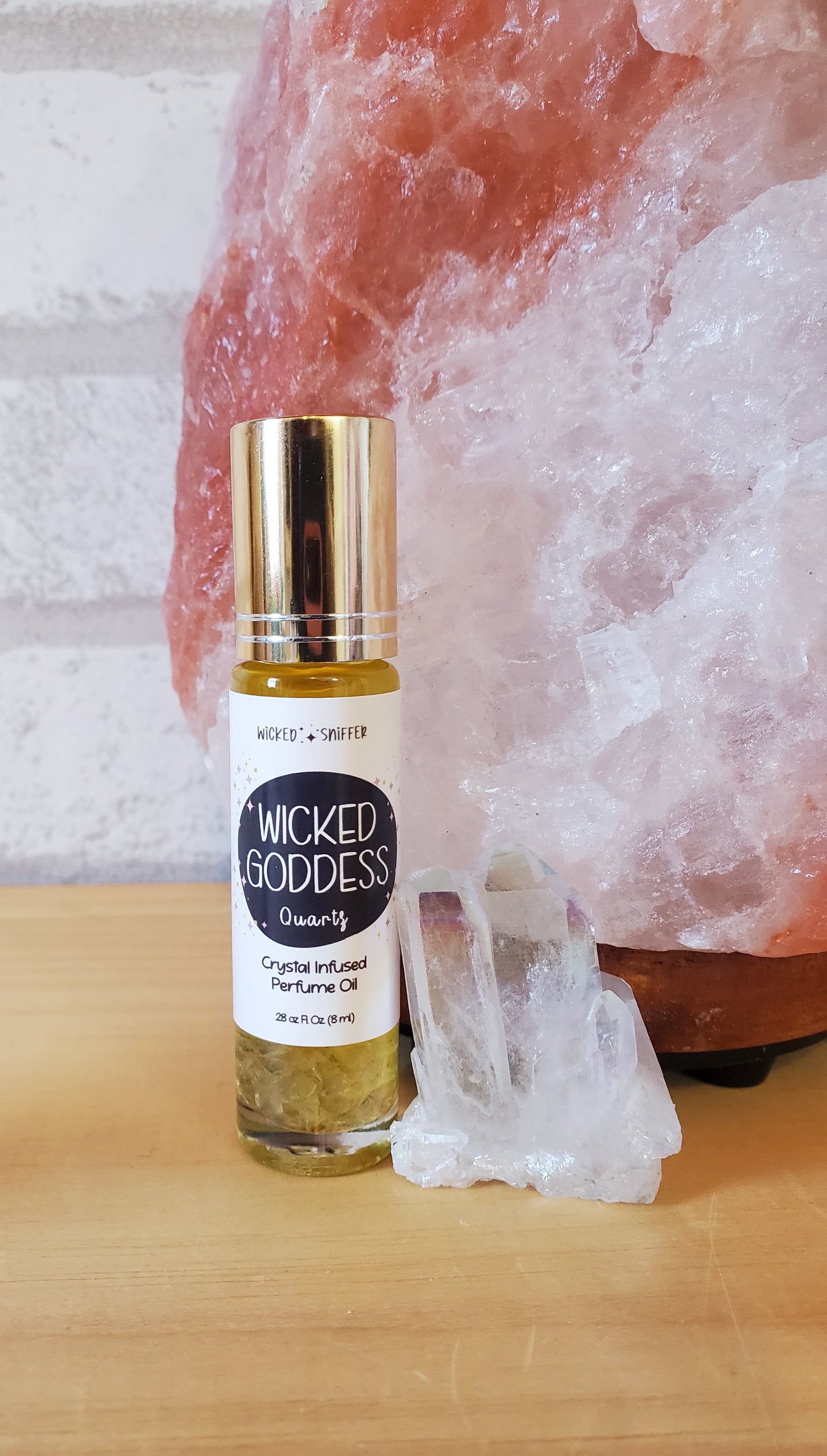 Bottle of 'Wicked Goddess' perfume oil on a wooden surface with a crystal in the background