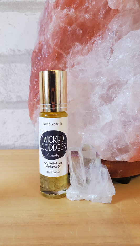 Bottle of 'Wicked Goddess' perfume oil on a wooden surface with a crystal in the background