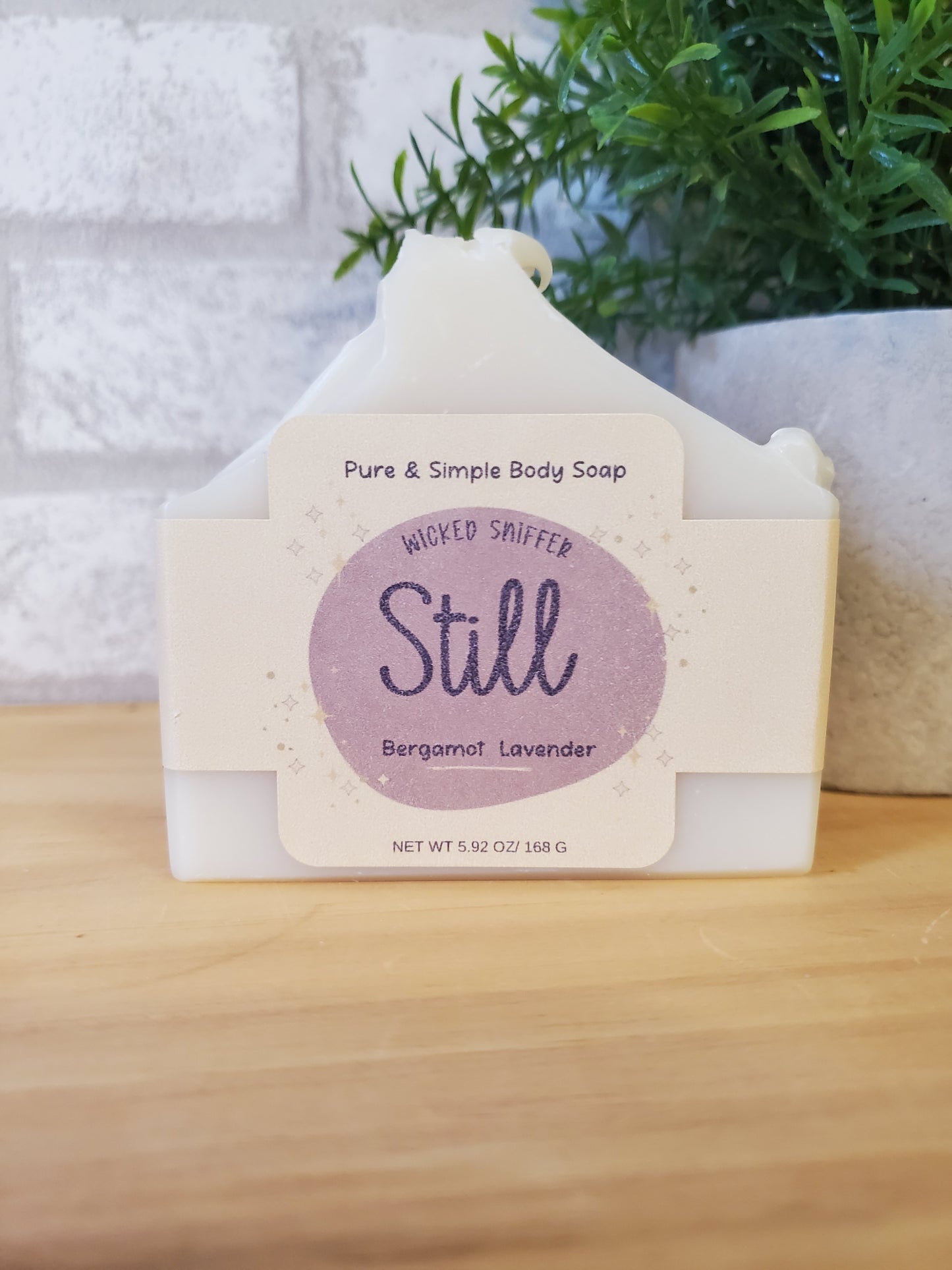 Bar of soap with a 'Still' label on a wooden surface with a plant in the background
