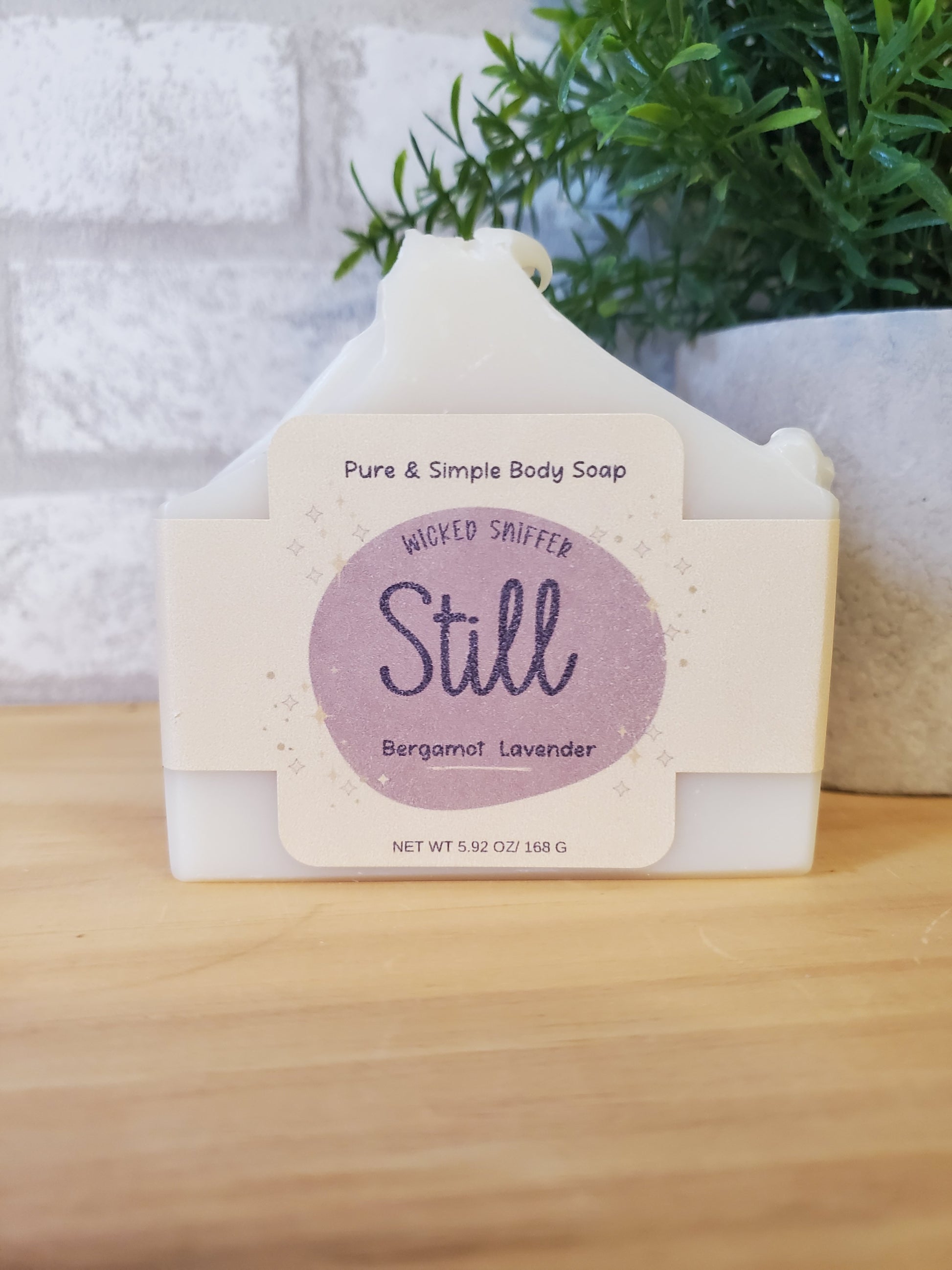 Bar of soap with a 'Still' label on a wooden surface with a plant in the background