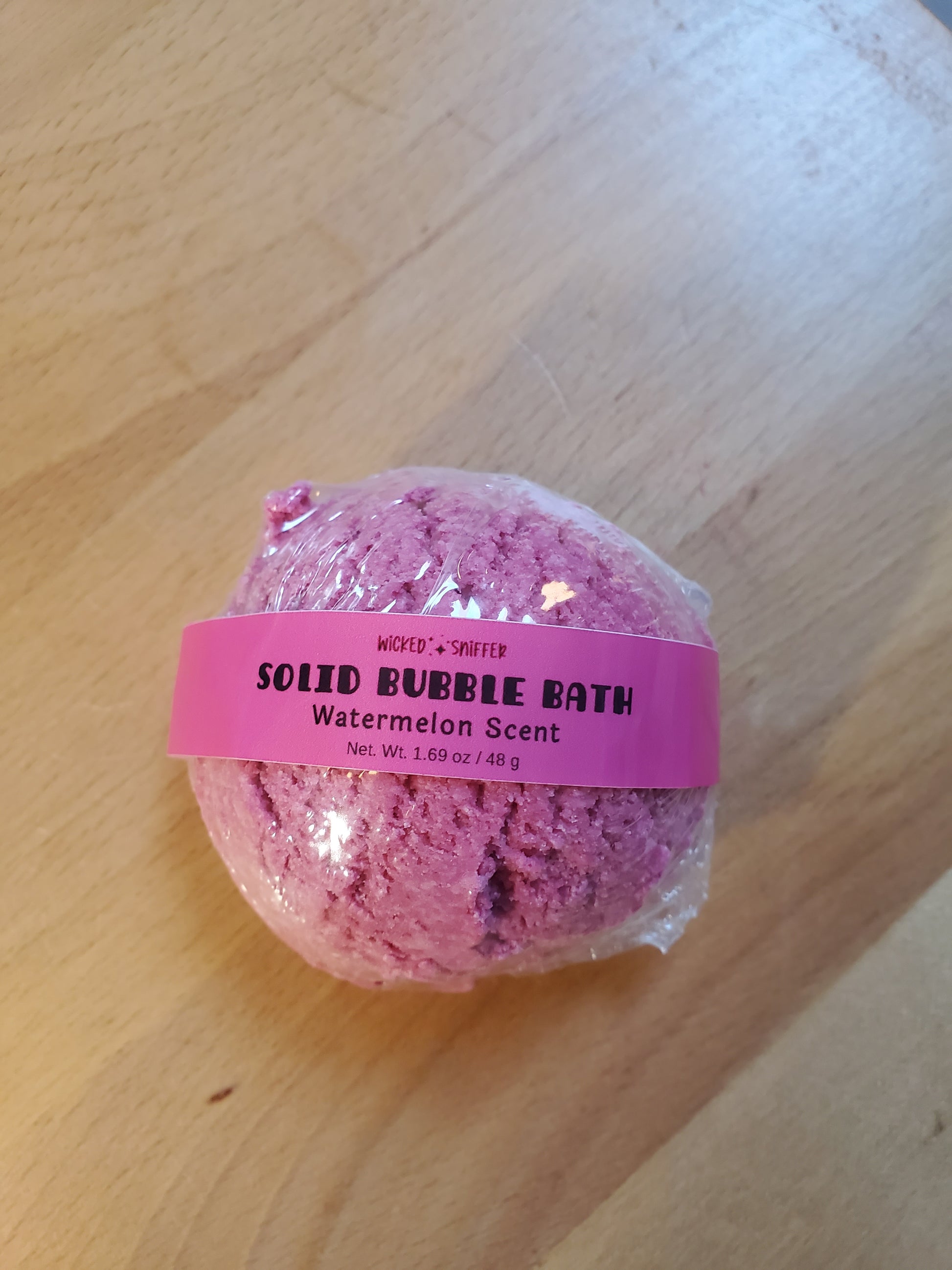 Pink bubble bath scoop with a label on a wooden surface