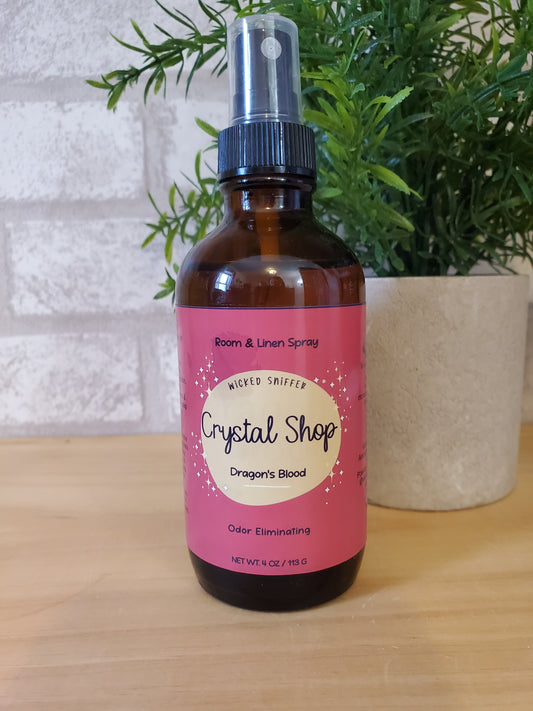 Bottle of room spray with a pink label on a wooden surface with greenery.