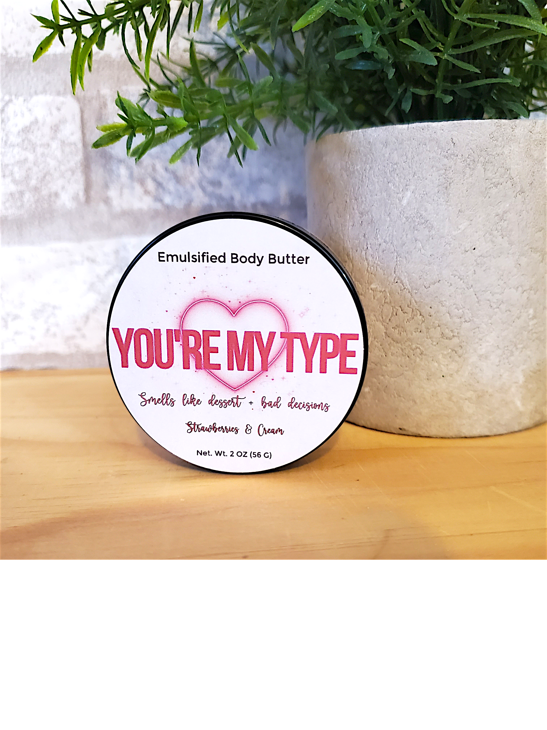 Body butter container with 'You're My Type' label next to a plant on a wooden surface