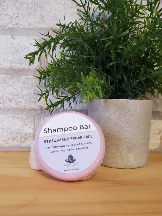 Shampoo bar with pink container on a wooden surface next to a plant