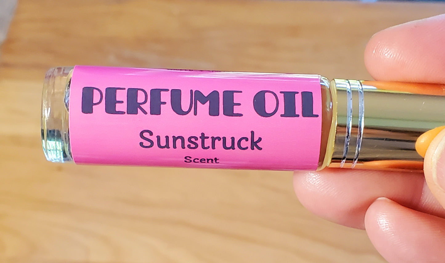 Perfume oil bottle labeled 'Sunstruck' held by a hand on a wooden surface