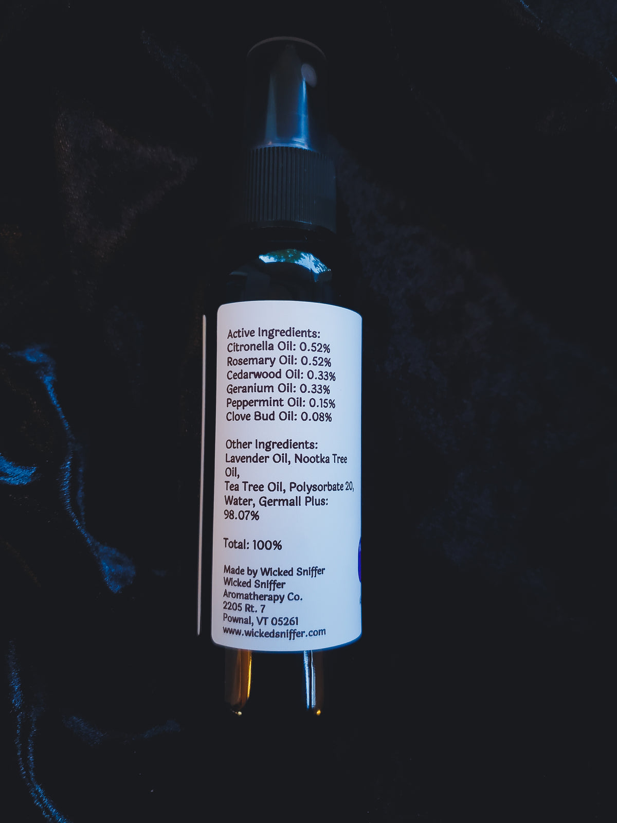 A black spray bottle with a white label showing active ingredients, photographed against a dark textured background.
