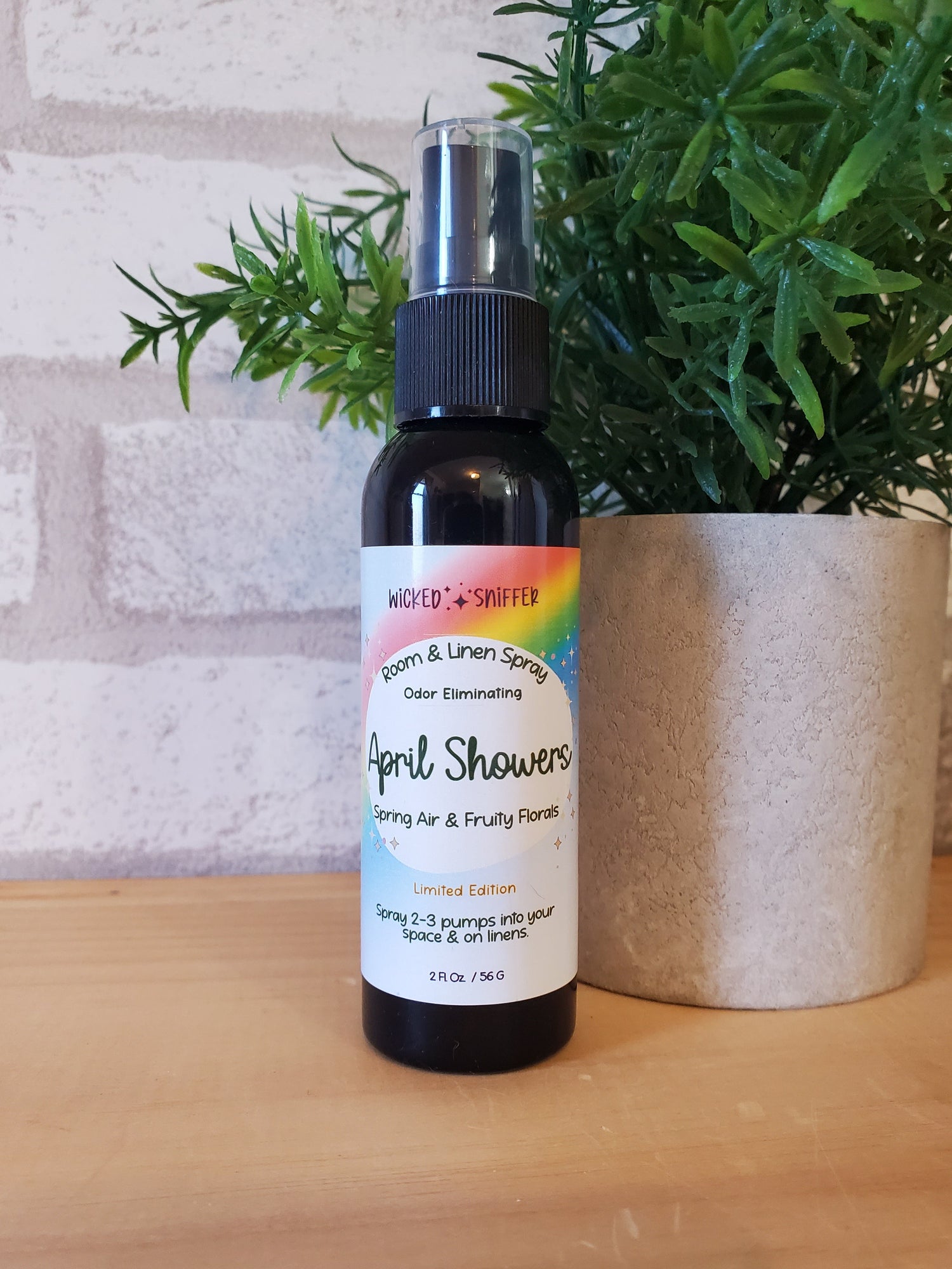 Bottle of April Showers soap with a rainbow label on a wooden surface next to a plant.