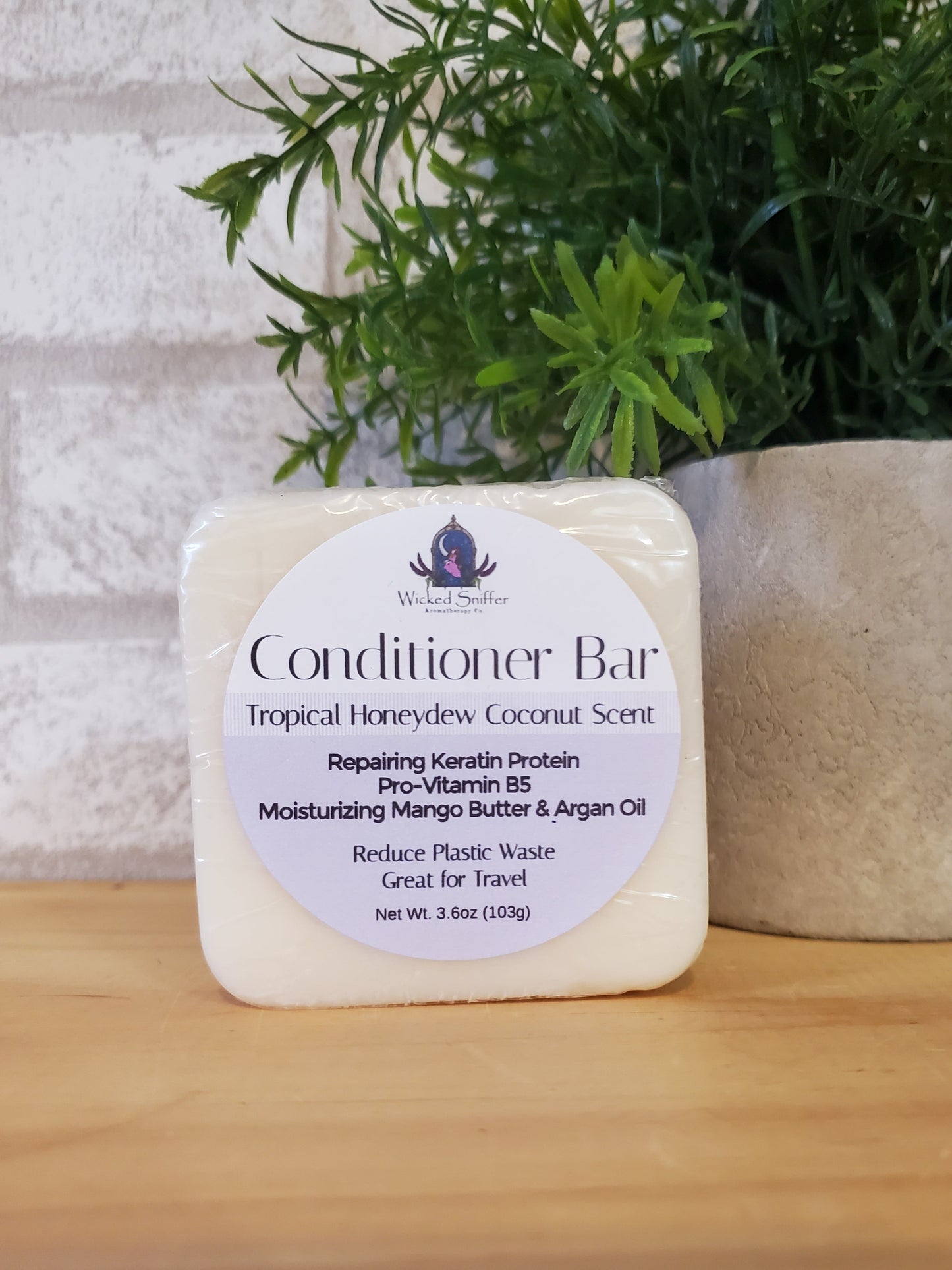 Bar of conditioner with a label on a wooden surface next to greenery