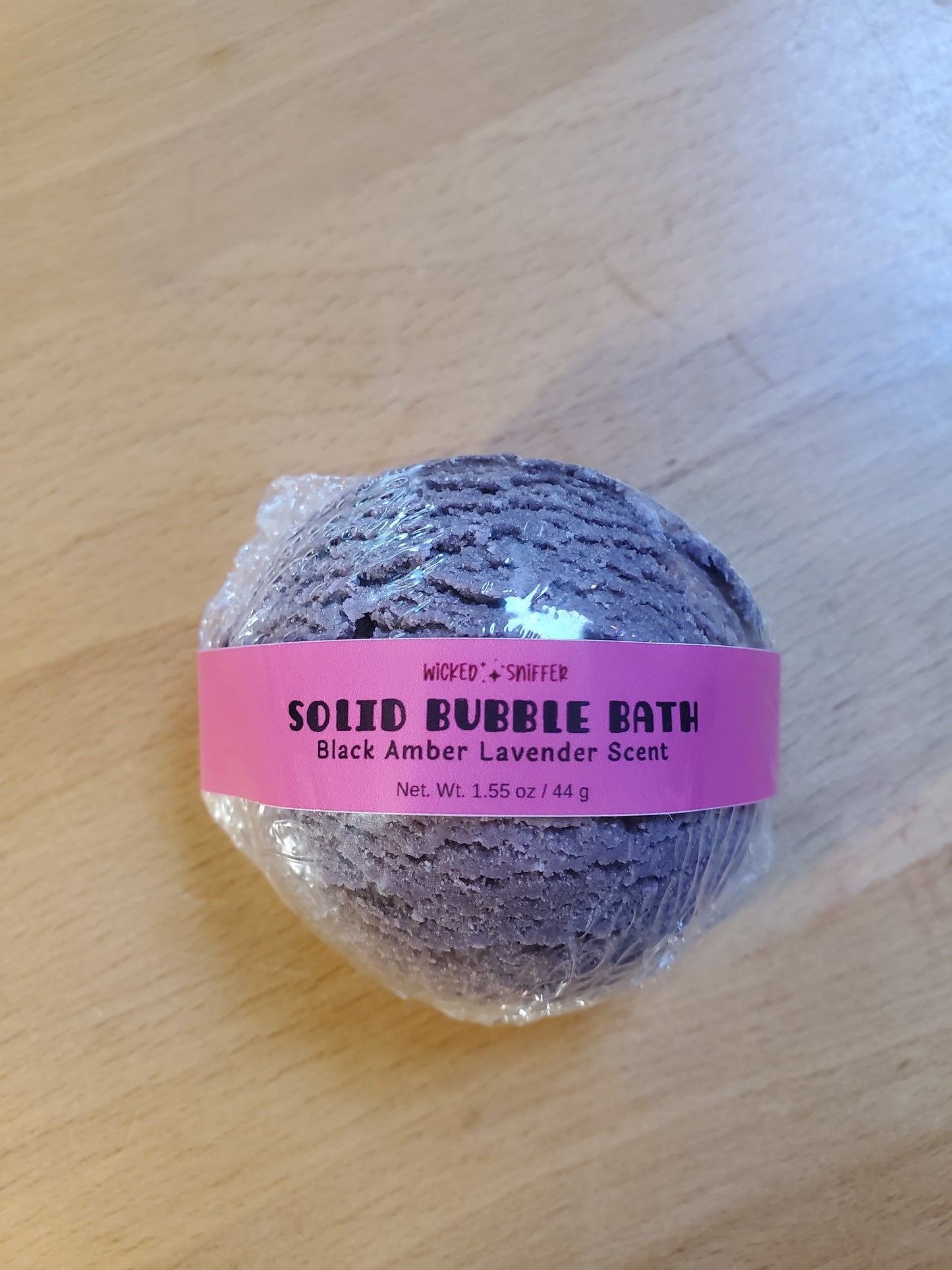 Solid bubble bath ball with a pink label on a wooden surface