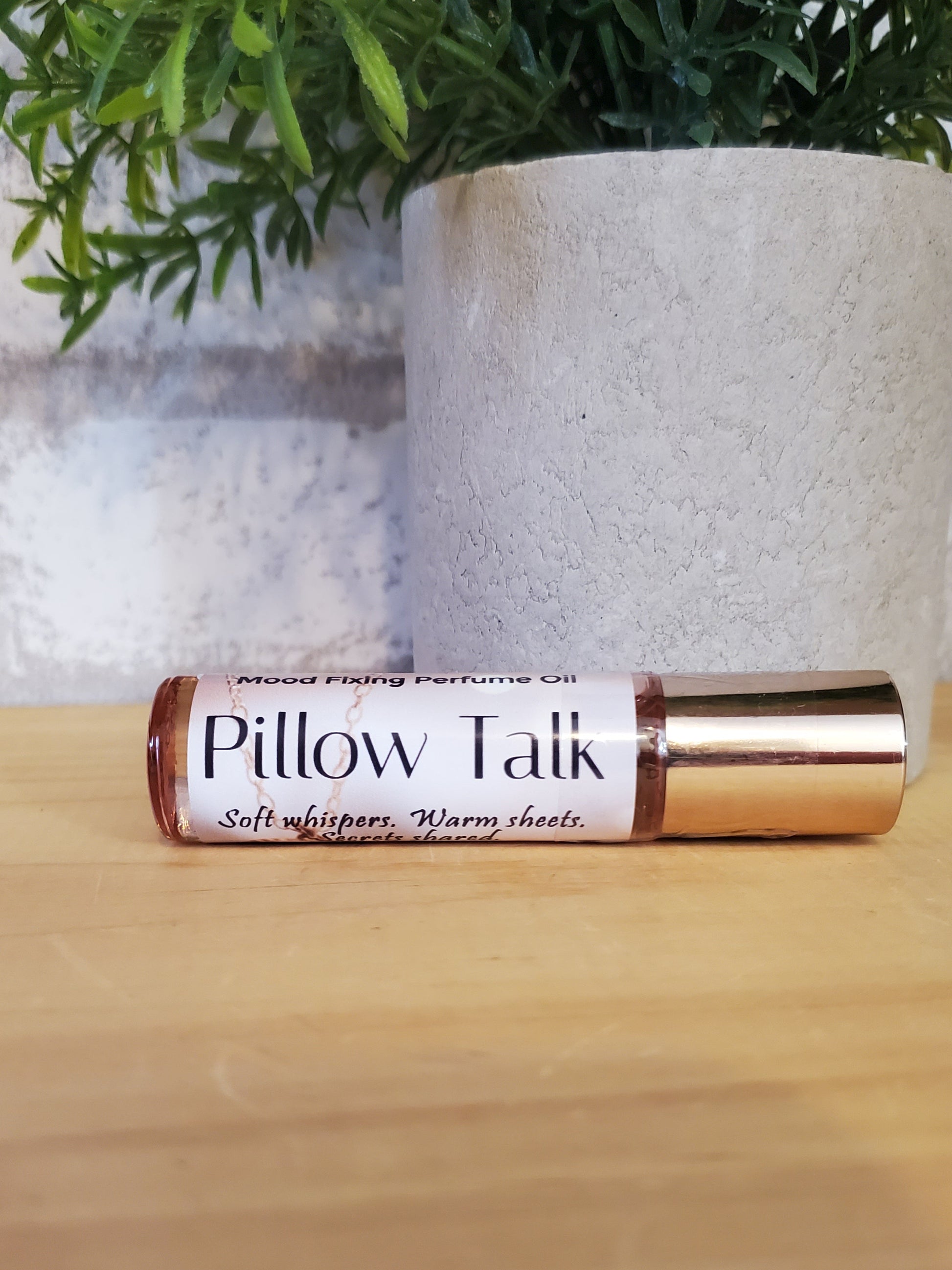 Pillow Talk rollerball on a wooden surface with a plant in the background