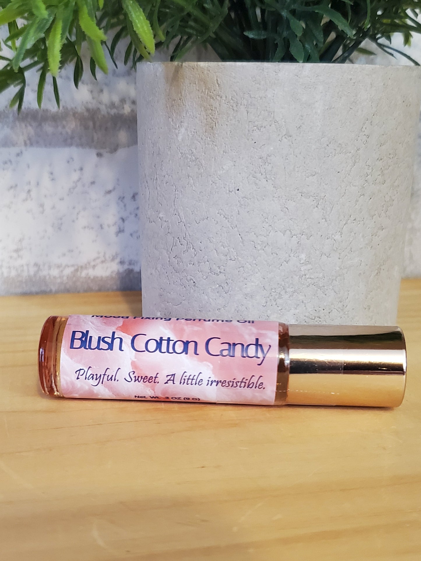 Roll-on bottle labeled 'Blush Cotton Candy' on a wooden surface with greenery in the background