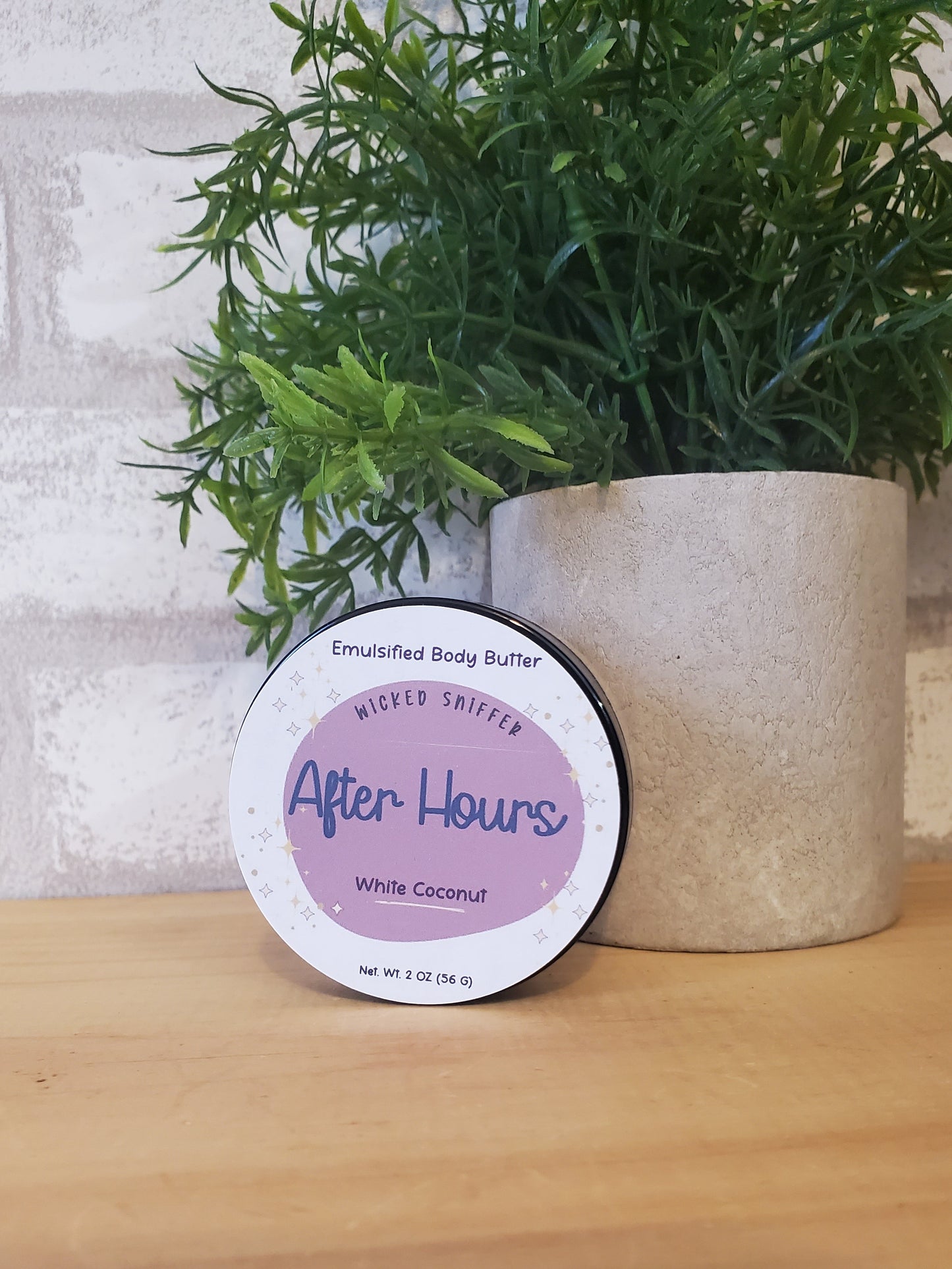 Jar of 'After Hours' body butter on a wooden surface with a plant in the background