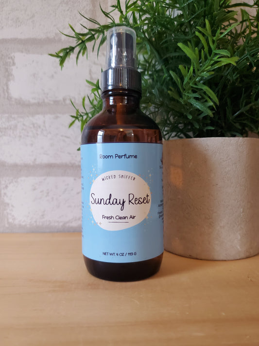 Bottle of room perfume with a label on a wooden surface next to greenery