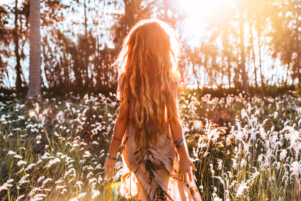 Young woman with long dreadlocks walking through a flower meadow.
