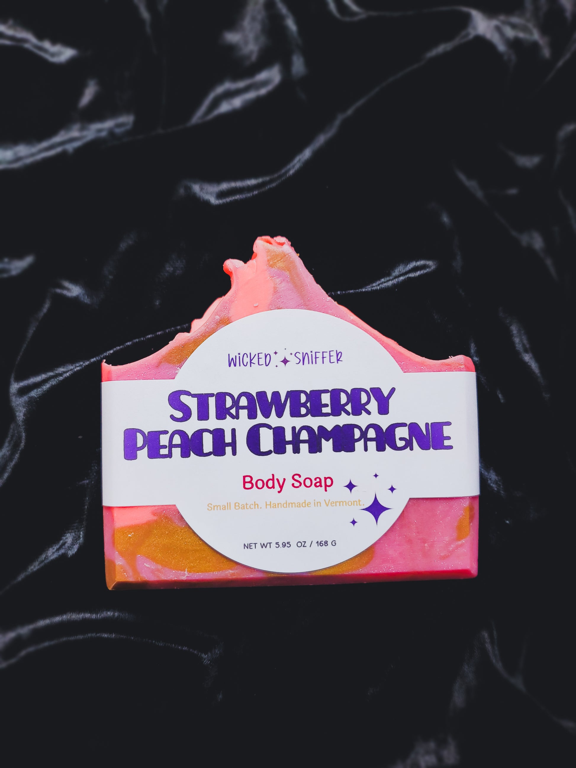 Bar of strawberry peach champagne body soap with a colorful label on a dark background